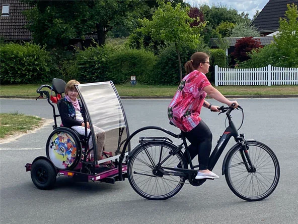 Maja mit ihren Eltern und ihrem Rollstuhlanhänger